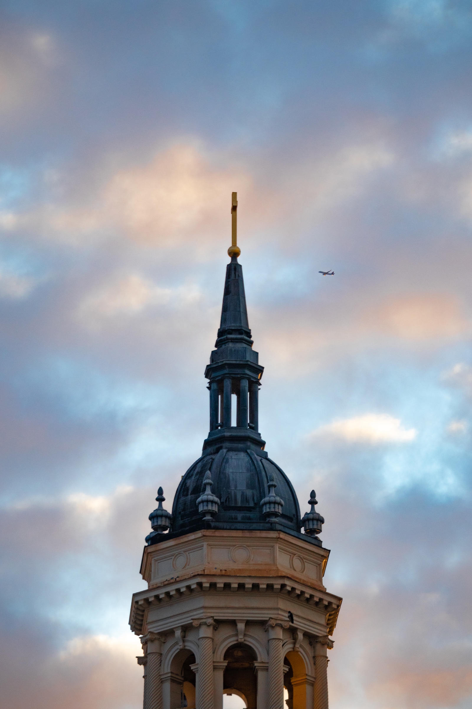 A church steeple against a cloudy sky with a plane passing