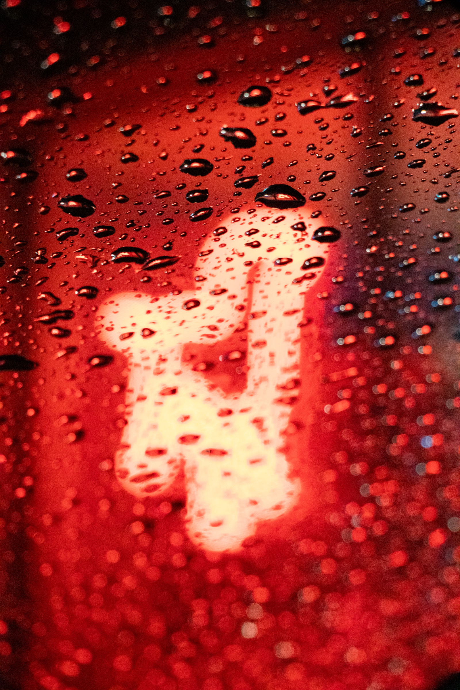 Raindrops on glass lit by a glowing neon sign