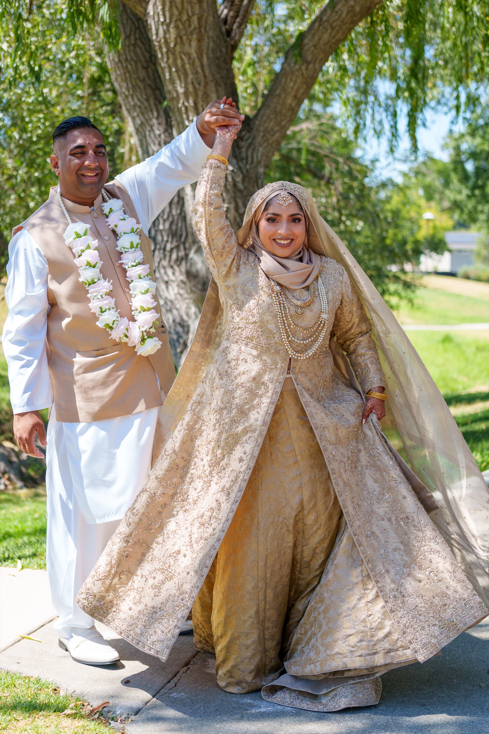 Newlyweds joyfully raising their hands together under a tree